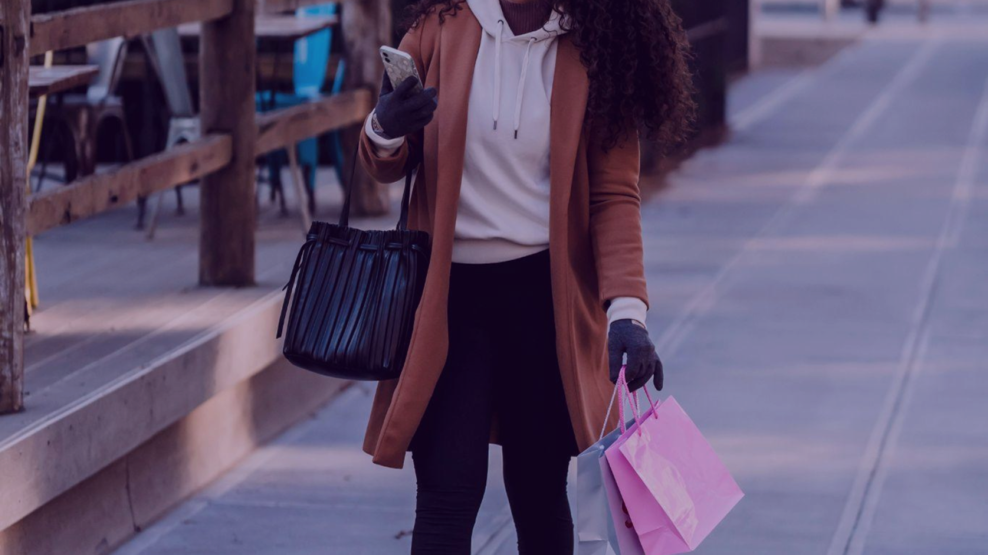 Foto de uma mulher com sacola de compras e um celular. A imagem transmite a ideia de compra local e incentiva o consumidor a buscar por lojas e serviços em sua região, por marketing local.